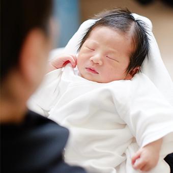 赤ちゃんの写真。赤ちゃんは白く柔らかい服に身を包まれ、大人の腕の中で眠っている。