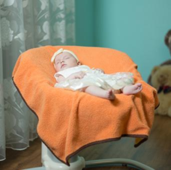 アームチェアで眠る赤ちゃんを撮影した写真。アームチェアにはオレンジ色の毛布が掛けられており、その上で白い服を着た赤ちゃんが眠っている。