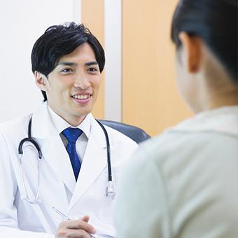 男性の医師を撮影した写真。医師は白衣を着て患者と向き合い、微笑んでいる。