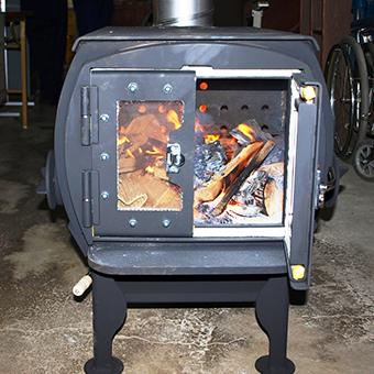 薪ストーブを撮影した写真。薪ストーブはグレーで開閉扉があり、扉を開けたストーブの中には炭が入っており、燃えている。